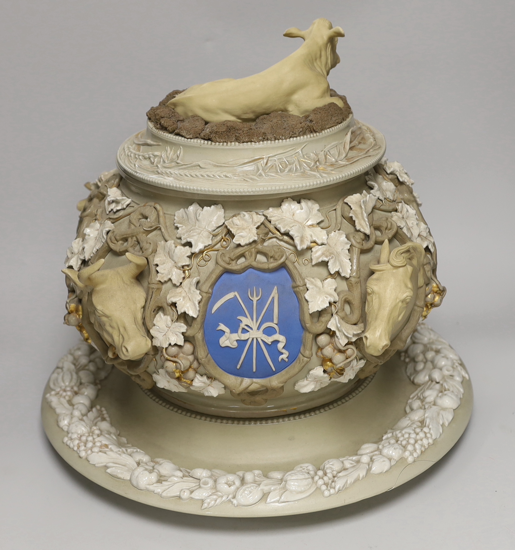 An impressive English cane ware and drab ware ‘agriculture’ soup tureen, cover and stand with cover, modelled with cattle, a dog and a horse’s head, amongst twining vines and crests, 38cm high